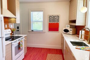A modern kitchen with white cabinetry, a built-in oven, a microwave, and a window with blinds.