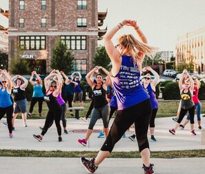 A group of people exercising outdoors in a public space with buildings in the background.