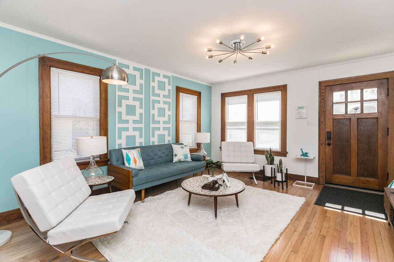 A living room with a blue sofa, white armchairs, a coffee table, and a wooden floor.
