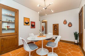 A dining area with a round table and four chairs, a wooden cabinet with glass doors, and a ceiling light fixture.