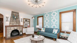 A living room with a stone fireplace, a blue sofa, a white armchair, and a round coffee table. - 1960s Gem-Close to Downtown & In a Quiet Area (Cedar Rapids)