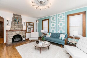 A living room with a stone fireplace, a blue sofa, a white armchair, and a round coffee table. - 1960s Gem-Close to Downtown & In a Quiet Area (Cedar Rapids)