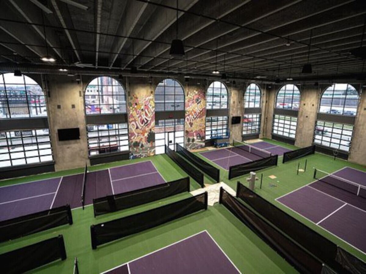 Un complexe de tennis intérieur doté de plusieurs courts, de grandes fenêtres et d’un plafond haut.