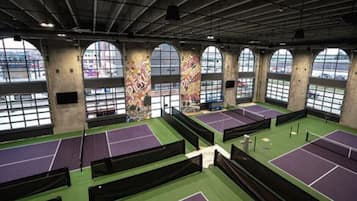 Un complexe de tennis intérieur doté de plusieurs courts, de grandes fenêtres et d’un plafond haut.