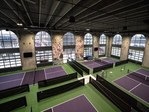 Eine Tennishalle mit mehreren Plätzen, großen Fenstern und Industrie-Architektur.