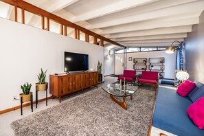 A modern living room with a TV, wooden cabinet, glass coffee table, red chairs, and a blue sofa.