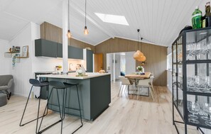 Une cuisine moderne dotée d’un îlot central, de tabourets de bar et d’un coin repas avec une table et des chaises en bois.