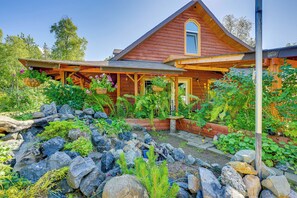 Une maison en bois avec un porche, entourée d’un jardin agrémenté de rochers et de plantes.