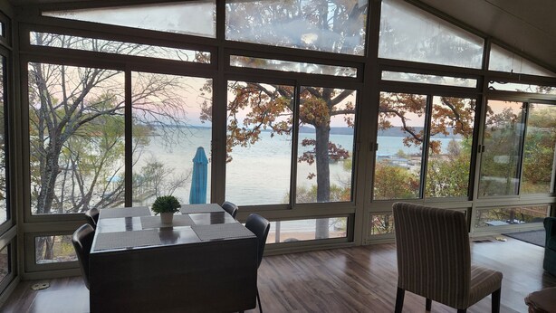 A room with large windows overlooking a body of water and trees. There is a table with chairs and a potted plant. - Waterfront Stay at Sandpiper Cove (Eufaula)