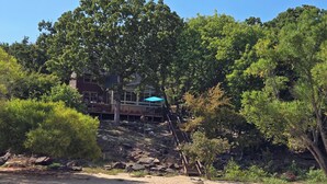 A riverside property with a wooden deck, a staircase leading to a building, and a sandy beach area. - Waterfront Stay at Sandpiper Cove (Eufaula)