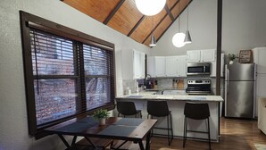 A modern kitchen with a wooden ceiling, a large window with blinds, a central island with bar stools, and a refrigerator. - Waterfront Stay at Sandpiper Cove (Eufaula)
