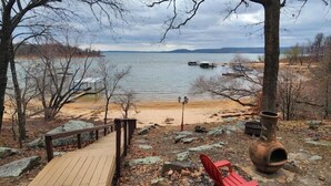 A wooden deck leading to a sandy beach with a view of a calm lake, boats, and distant hills. - Waterfront Stay at Sandpiper Cove (Eufaula)