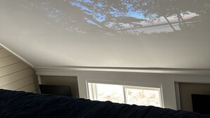 Ein Zimmer mit schräge Decke und Dachfenster, durch das ein Blick auf einen Baum möglich ist.