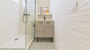 A modern bathroom with a glass-enclosed shower, a wooden vanity with a mirror, and a patterned floor. - Le Tarnosien - Landes - Côte Basque (Tarnos)