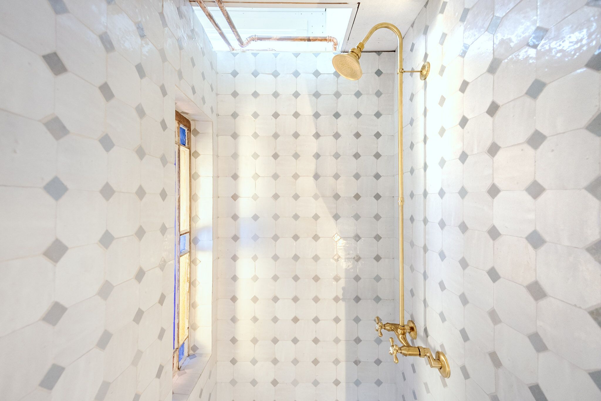 A bathroom with white hexagonal tiles, a skylight, and a gold shower fixture.