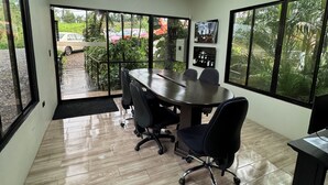A conference room with a large table, black office chairs, and large windows offering a view of the outdoors.