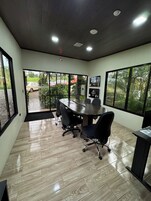 A conference room with a large table, black office chairs, and large windows offering a view of the outdoors.