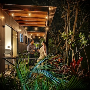 A modern outdoor seating area with wooden beams and string lights, surrounded by lush greenery and plants. - Boutique Hotel Containers (Florencia)