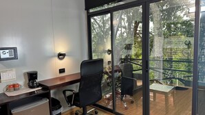 A modern office space with a desk, chair, and a view of a balcony with outdoor furniture.