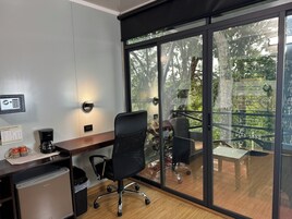 A modern office space with a desk, chair, and a view of a balcony with outdoor furniture.