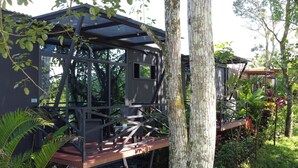 A modern outdoor seating area with a glass enclosure, surrounded by lush greenery and trees.