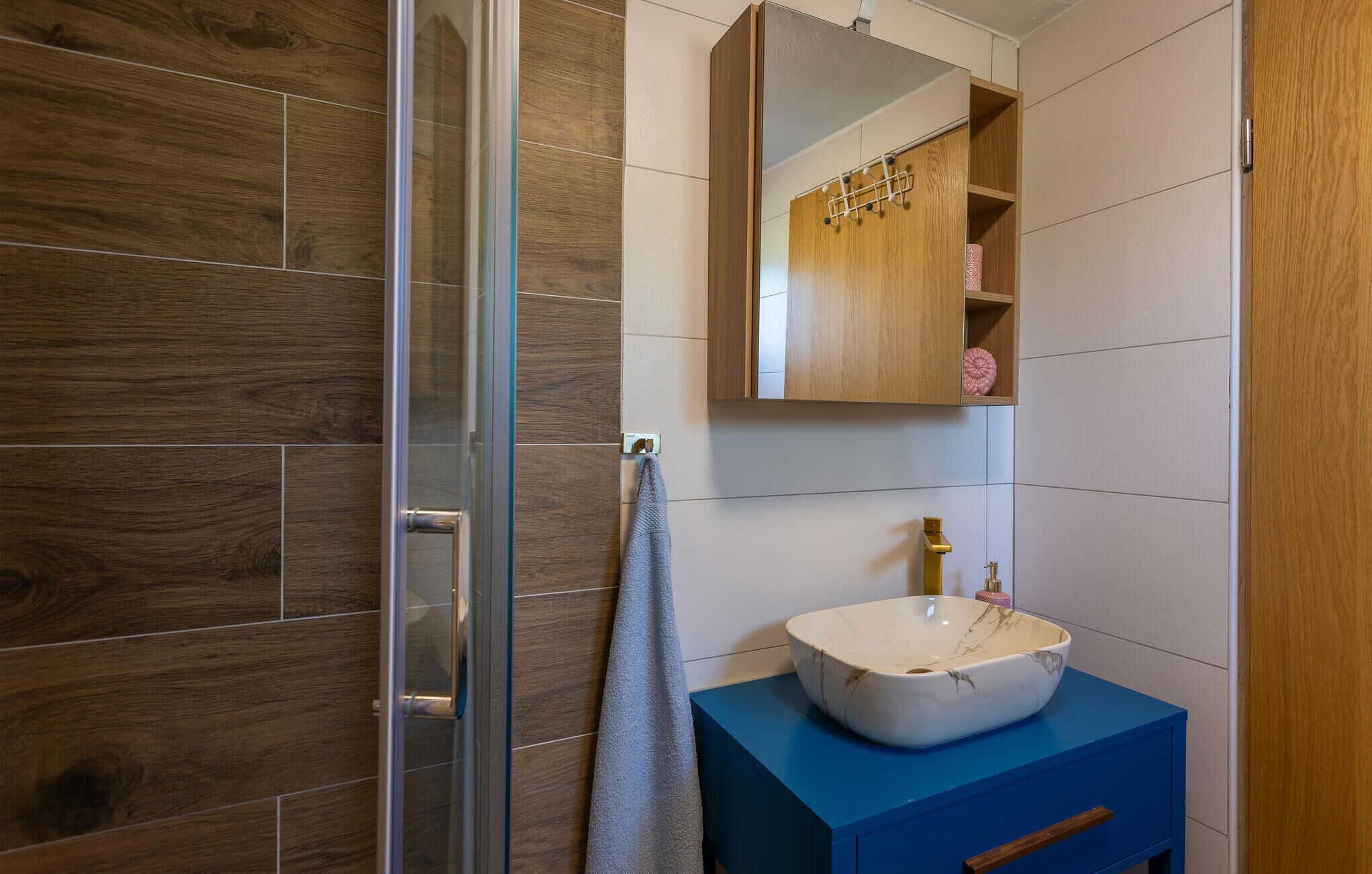 A bathroom with a glass shower door, a white sink with a marble-like design, and a blue vanity.
