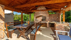 Une terrasse extérieure dotée d’un four en briques, de bancs en bois et d’un espace barbecue.