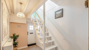 Un escalier avec des marches blanches menant à un palier, une porte avec une fenêtre et un tableau accroché au mur.