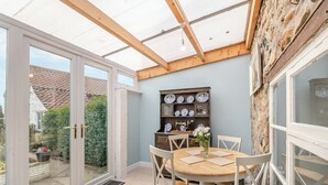 Une véranda avec un plafond en bois, une table à manger avec des chaises et une bibliothèque agrémentée d’assiettes décoratives.