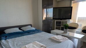 A modern hotel room with a bed, a TV, a desk, and a chair.
