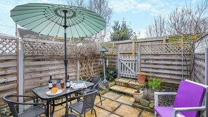 En udendørs terrasse med et bord, stole, en grøn parasol og et træhegn.