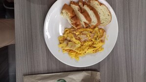 A breakfast plate with scrambled eggs, toast, and cantaloupe on a wooden table. - Casa Hotel Mared (Bogotá)