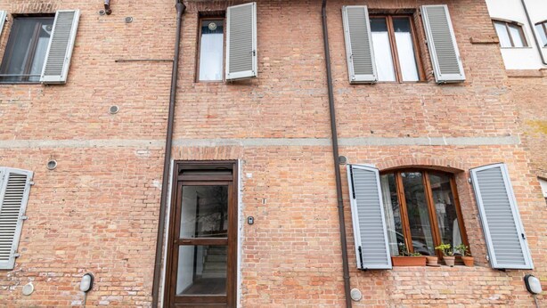 Un edificio de ladrillo con múltiples ventanas, algunas con contraventanas, y una puerta con paneles de vidrio.
