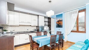 Una cocina moderna con armarios blancos, una mesa de comedor con sillas, piso de madera y una cama con colcha estampada.