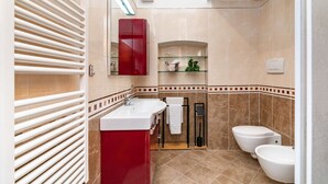 Un baño moderno con un armario rojo, un lavabo blanco, un estante de vidrio, un inodoro y una zona de ducha.