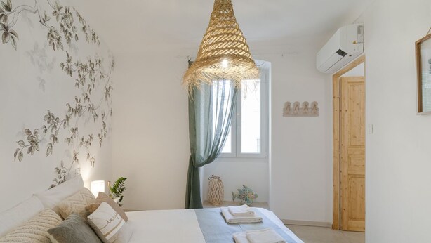A bedroom with a bed, a hanging light fixture, a window with curtains, a wall-mounted air conditioner, and a wooden door. - GuestHost - Spacious and elegant, finely renovated apartment capable of accommodating up to 6 people, located on the ground floor of a typical ligurian building in the center of Sanremo, a few steps from the famous Casino. Nearby is Via Matteotti, with i (Sanremo)