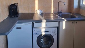 Una cocina compacta con lavadora, cafetera y fregadero.