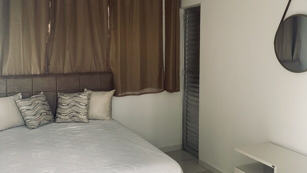 Un dormitorio con cama, cortinas, mesita de noche y espejo.