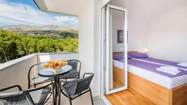 Ein Balkon mit Tisch und Stühlen, ein Bett mit lila Bettdecke und Blick auf eine Berglandschaft.