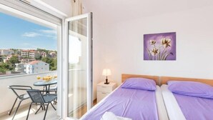 Ein Hotelzimmer mit Balkon, einem Bett mit lila Bettwäsche, einem Nachttisch mit Lampe und einem Blumenbild an der Wand.