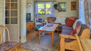 A cozy living room with a wooden sofa, a small table, a television, and a window with curtains.