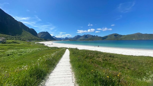 A coastal path leading to a beach with mountains in the background.