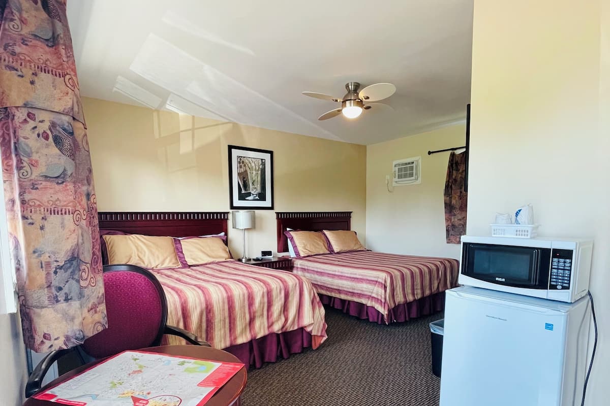 A hotel room with two beds, a desk with a map, a microwave, and a ceiling fan.