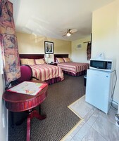 Habitación de hotel con dos camas, un escritorio con un mapa, microondas y ventilador de techo.