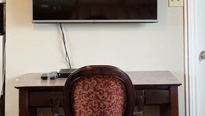A flat-screen TV mounted on a wall above a wooden desk with a patterned chair. - Scenic Motel Moncton  (Berry Mills)
