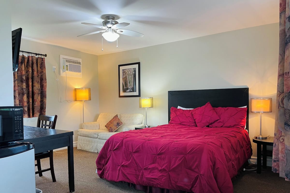 A hotel room with a bed, a desk, a chair, a ceiling fan, and two wall-mounted lamps.