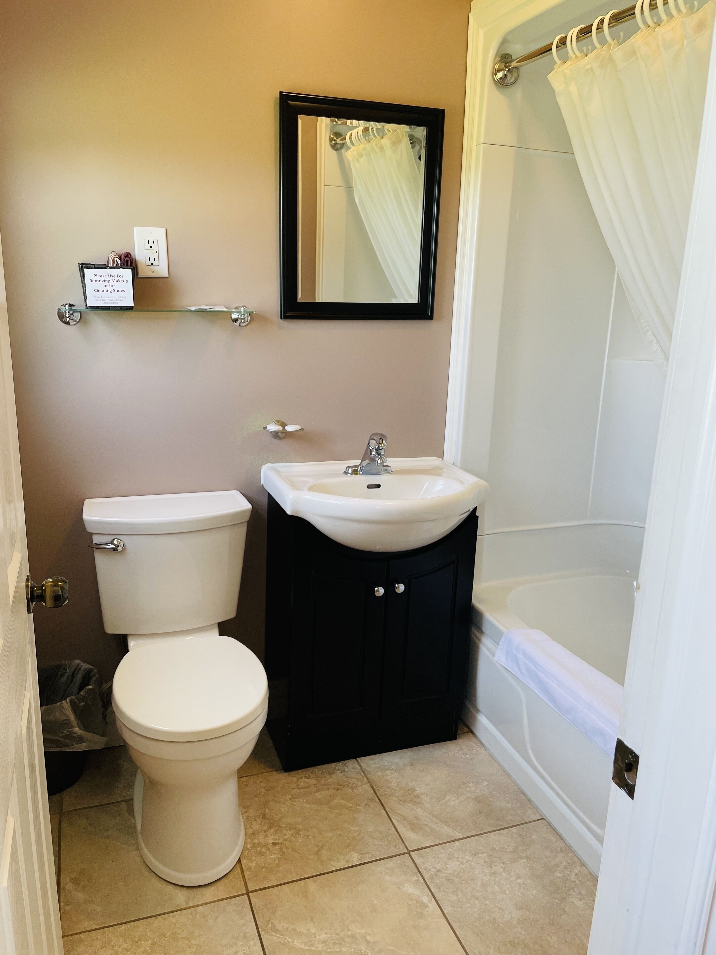 A bathroom with a toilet, sink, and bathtub. There is a mirror above the sink and a shower curtain over the bathtub.