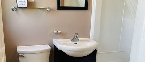 A bathroom with a toilet, sink, and bathtub. There is a mirror above the sink and a shower curtain over the bathtub.