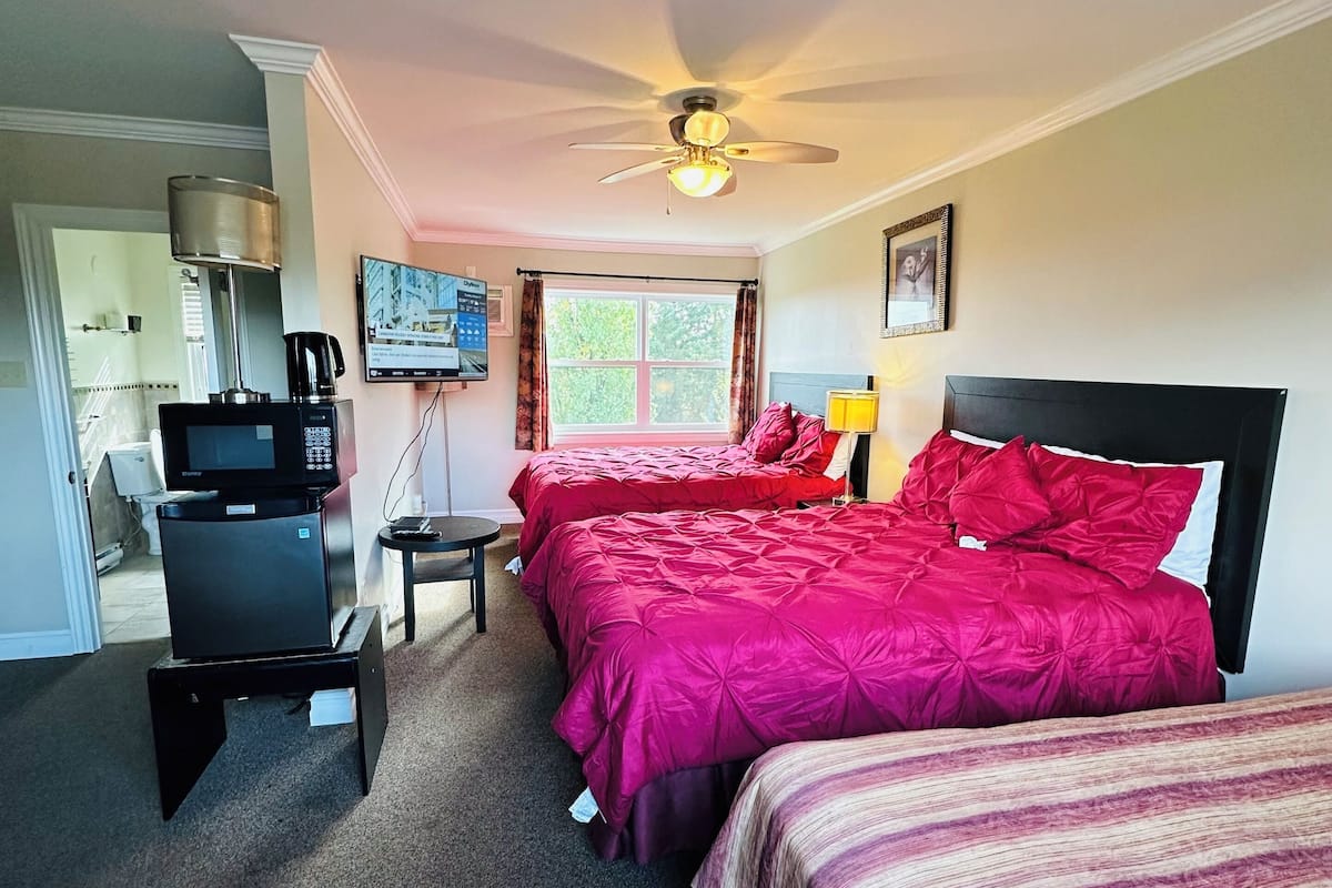 A hotel room with two beds, a desk, a ceiling fan, a TV, and a window with curtains.