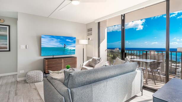 Ein modernes Wohnzimmer mit großem Fernseher, bequemen Sitzmöbeln und einem Balkon mit Blick auf die Stadt.